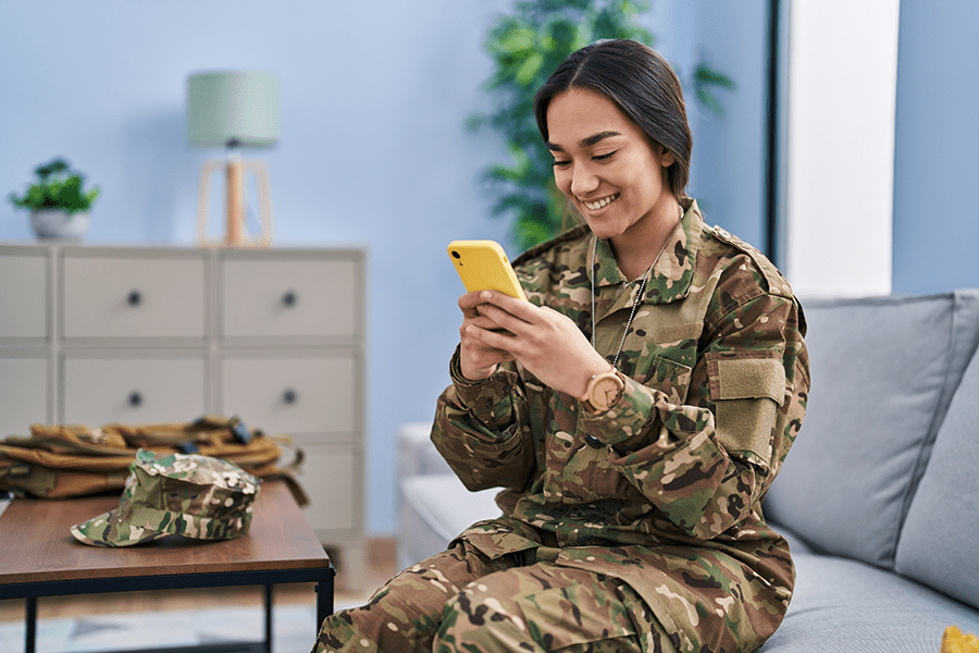 Smiling military woman in camo checking phone in cozy furnished apartment; NIKA's MacDill AFB TDY housing.