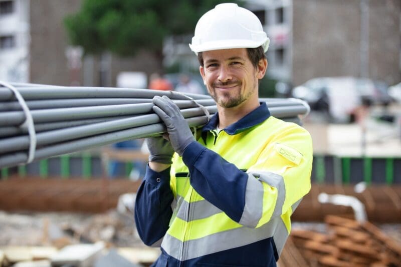 Construction worker carrying pipes at Abilene TX site, supported by NIKA's crew lodging.